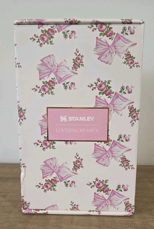 A Stanley Loveshackfancy gift box featuring a pink and green floral bow pattern on a white background, with a pink central label displaying the Stanley brand.