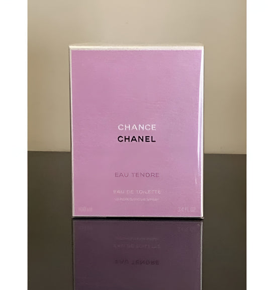 Chanel Chance Eau Tenore Eau De Toilette box in a lavender purple color, standing on a dark reflective surface against a beige wall.