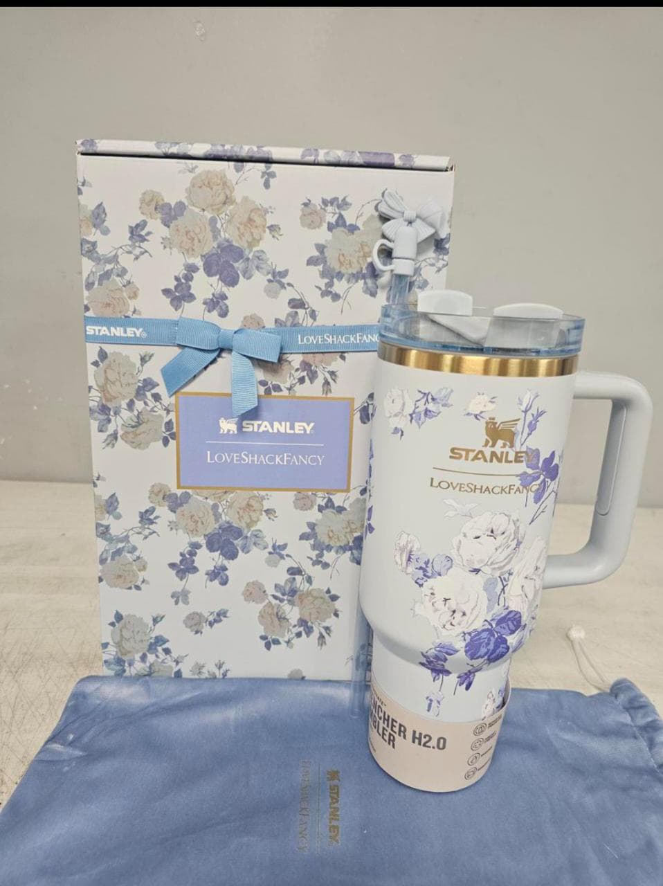 Stanley Love Shack Fancy insulated travel mug with floral print, shown next to its matching floral gift box and a blue drawstring bag on a neutral background.