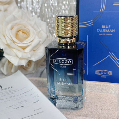 A rectangular glass perfume bottle labeled 'ILLOGO PARIS BLUE TALISMAN EAU DE PARFUM' stands on a tabletop, with a matching blue box behind it and a white rose in the background.