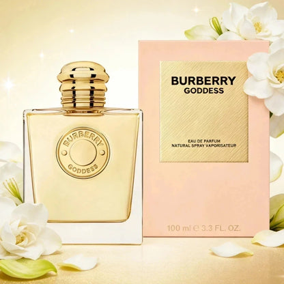 Burberry Goddess Eau de Parfum bottle with a gold cap next to its pink packaging box, decorated with white flowers on a warm beige background.