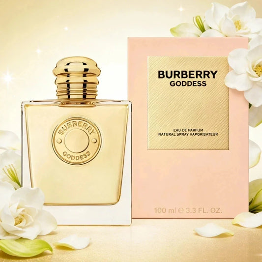 Burberry Goddess Eau de Parfum bottle with a gold cap next to its pink packaging box, decorated with white flowers on a warm beige background.
