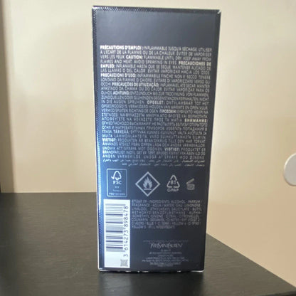 The back of a dark navy or black rectangular product box with dense white text, recycling symbols, and a barcode, standing on a dark tabletop against a beige wall.