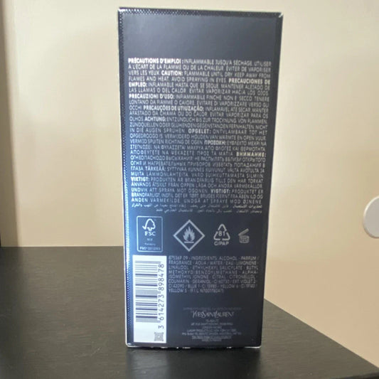 The back of a dark navy or black rectangular product box with dense white text, recycling symbols, and a barcode, standing on a dark tabletop against a beige wall.