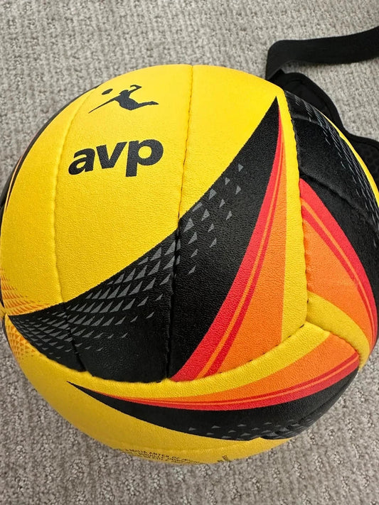A yellow handball with black and orange-red graphic patterns and the brand name 'avp' printed on it, resting on a gray textured carpet.