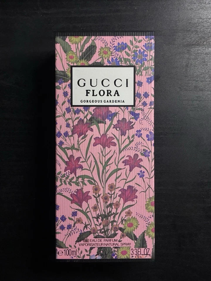 Gucci Flora Gorgeous Gardenia Eau de Parfum 100ml box, featuring a pink floral pattern with purple and green botanical illustrations, set against a dark background.