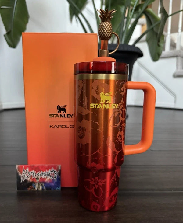 Red Stanley mug with an orange handle and pineapple spout on a wooden surface.