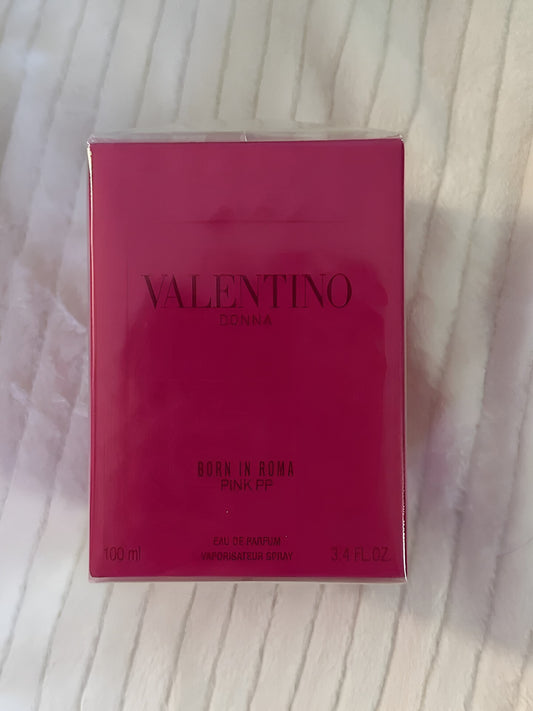 A 100ml box of Valentino Donna Born in Roma Pink FF Eau de Parfum, featuring a vibrant pink box with black lettering, placed on a white textured fabric background.